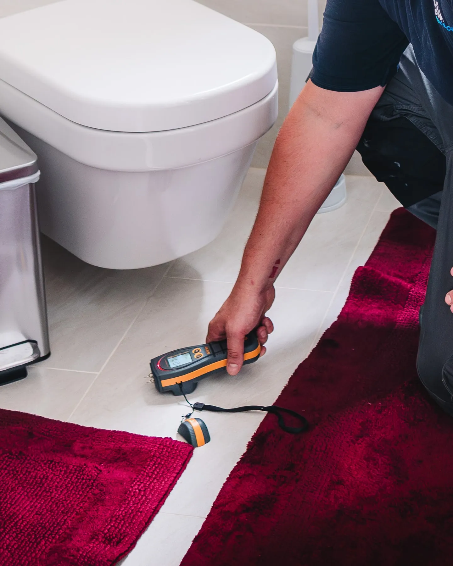 ADI engineer taking a moisture reading on pale bathroom floor tiles beside a toilet